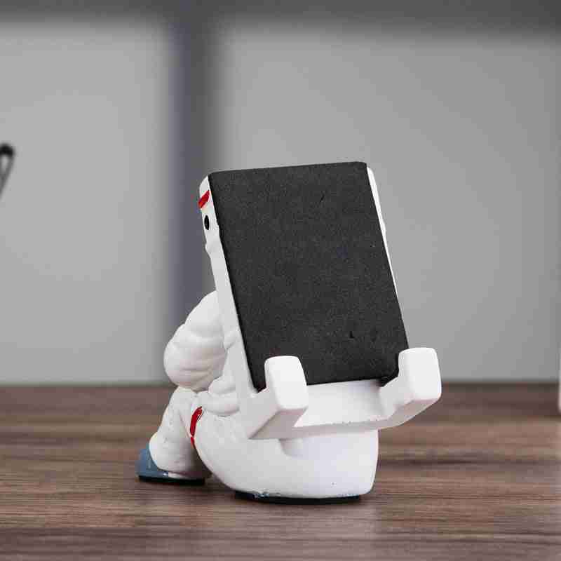 Astronaut Mobile Phone Stand Fun & Functional Desk Holder made of resin, featuring a seated astronaut figure holding a remote and supporting a smartphone.