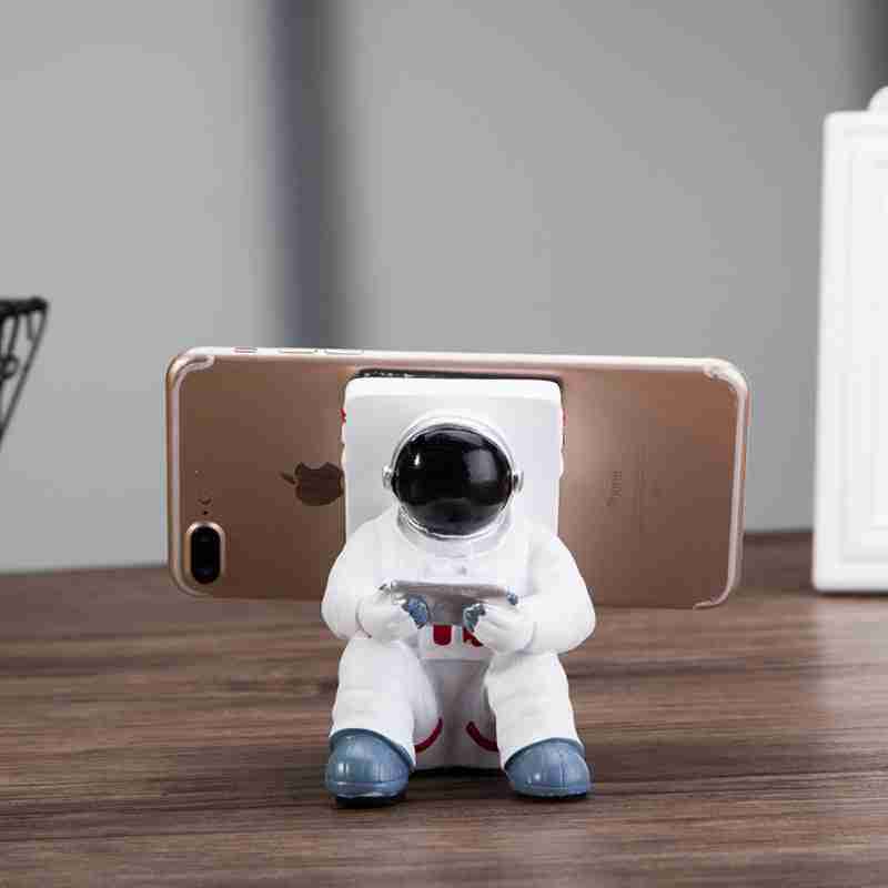 Astronaut Mobile Phone Stand Fun & Functional Desk Holder made of resin, featuring a seated astronaut figure holding a remote and supporting a smartphone.