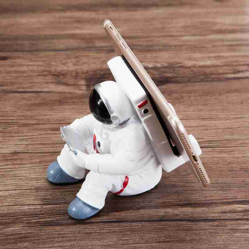 Astronaut Mobile Phone Stand Fun & Functional Desk Holder made of resin, featuring a seated astronaut figure holding a remote and supporting a smartphone.