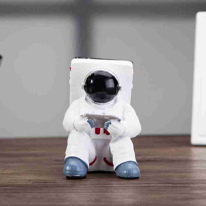 Astronaut Mobile Phone Stand Fun & Functional Desk Holder made of resin, featuring a seated astronaut figure holding a remote and supporting a smartphone.