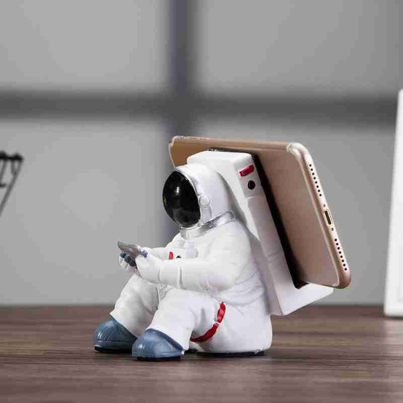 Astronaut-shaped resin mobile phone stand holding a smartphone, stylish and durable design.